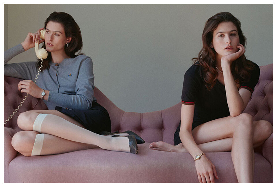 Two women seated on a pink sofa, both wearing Vivienne Westwood watches; one holds a vintage telephone.